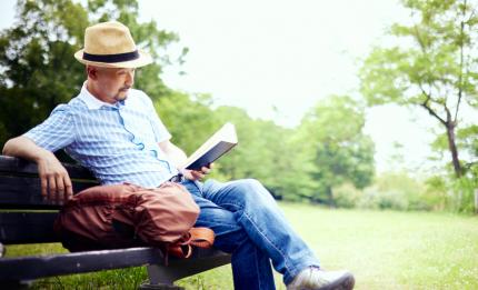 Man reading a book sat on a bench outside